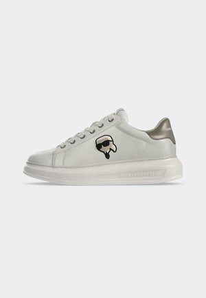 Weißer Sneaker mit dicker Sohle, grauer Fersenschlaufe und einem kleinen Cartoon-Gesicht mit Sonnenbrille an der Seite.