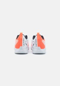 Scarpe sportive con un design bianco e arancione, dotate di una tomaia testurizzata, dettagli neri e un tallone prominente per facilitare l'indossamento.
