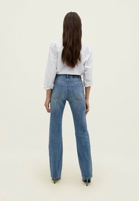 Jeans azzurri a vita alta con taglio dritto, dotati di un design a cinque tasche e dettagli di cucitura sottili, indossati con una blusa bianca.