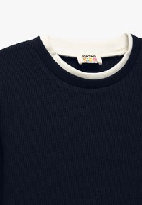 Marineblå waffle-strikket langærmet skjorte med en kontrastfarvet creme ribbet crew neckline og et mærke, der siger "Koton Kids."