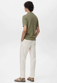 Polo shirt verde oliva con un tessuto a maglia testurizzato, abbinato a pantaloni beige chiari e sandali marroni, visto da dietro.