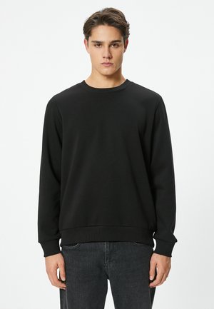 Svart sweatshirt med rund hals, långa ärmar och ribbade ärmslut. Tillverkad av ett tyg med slät textur och har en avslappnad passform.