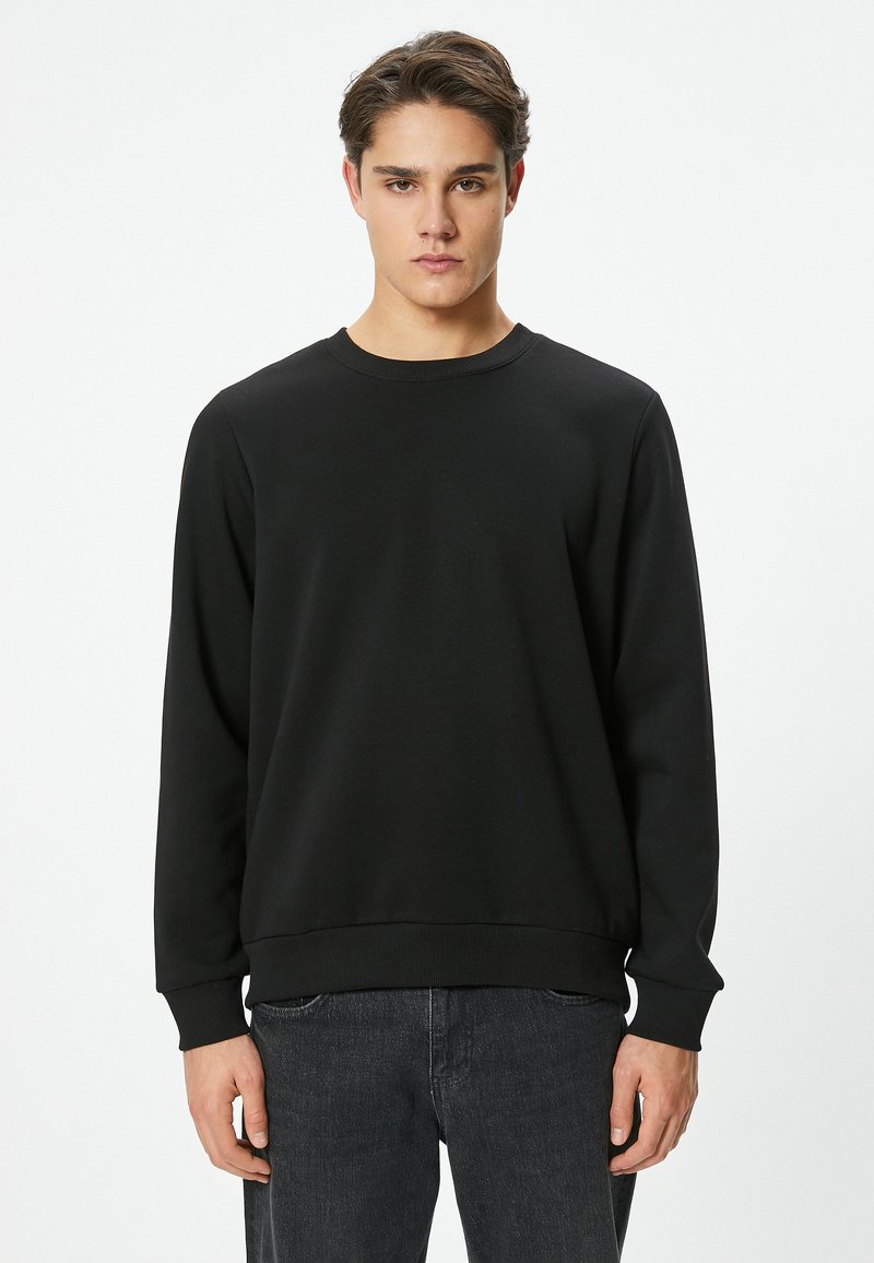 Sudadera negra con cuello redondo, mangas largas y puños acanalados. Confeccionada con un tejido de textura suave, presenta un diseño de corte holgado.