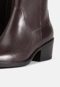 Bottine en cuir brun foncé avec petit talon bloc et fermeture éclair latérale visible, texture lisse et coutures détaillées.