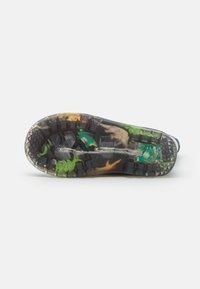 Semelle de chaussure présentant un design à motifs avec des sections en caoutchouc transparent révélant des couleurs vives vertes, jaunes et noires, texturée pour offrir une adhérence.