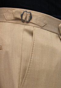 Κοντινό πλάνο μπεζ παντελονιού με ρυθμιζόμενο πλαϊνό κούμπωμα και λεπτομερές ράψιμο στη μέση και την άκρη της τσέπης.