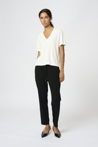 T-shirt bianco con scollo a V, maniche corte, abbinato a pantaloni neri con cordino. Ballerine nere a punta completano l'outfit. Linee semplici e pulite.