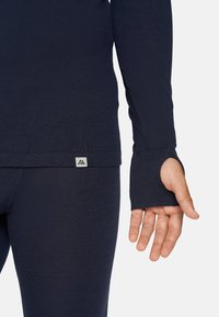 Marineblaues Langarmoberteil mit tailliertem Design, das Daumenlöcher an den Bündchen und ein kleines Logotag am Saum aufweist. Strukturierter Strickstoff.