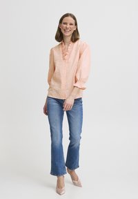 Peach button-up shirt with ruffled collar, 3/4-length sleeves, paired with light blue flared jeans and pale pink pointed heels.