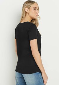 Maglietta nera a maniche corte con design aderente, realizzata in cotone leggero, con scollo rotondo e una texture liscia.