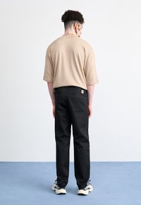 Beige kortærmet skjorte parret med sorte bukser. Skjorten har en afslappet pasform, mens bukserne har to baglommer og et logo-tag.