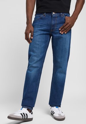 Dark blue denim jeans with a straight cut, featuring front pockets and a zipper fly. Worn with black and white athletic shoes.