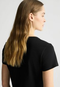 Zwarte katoenen t-shirt met een ronde halslijn en korte mouwen, gezien vanaf de achterkant, met een gladde textuur en een minimalistisch ontwerp.
