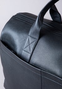 Black textured leather bag with dual top handles and stitched details, featuring a zippered opening and smooth finish for durability.