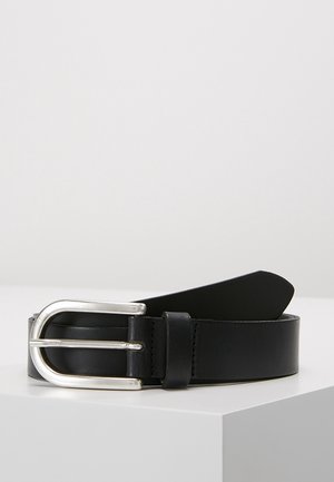 Ceinture en cuir noir avec boucle métallique argentée arrondie reposant sur une surface blanche contre un fond uni.
