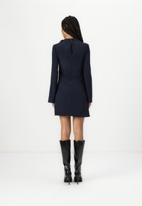 Jūras spēku garās piedurknes kleita ar pieguļošām siluetēm un aizmugurējo rāvējslēdzēju, apvienota ar elegantiem melniem ceļgala zābakiem. Gluda tekstūra.