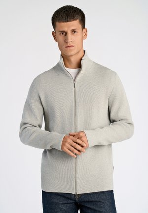 Grau gerippter Reißverschluss-Cardigan mit hohem Kragen, weichem Material und langen Ärmeln, getragen über einem weißen Hemd, kombiniert mit dunklen Jeans.