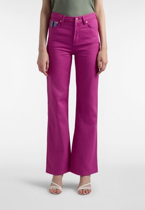 Lyserøde udvidede jeans med frontlommer, med et farverigt stribet detalje på lommen. Glat denimsstruktur. Standard linning med knap.