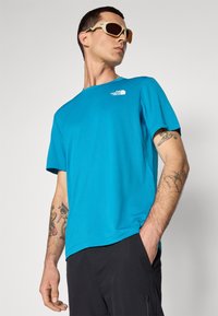 Niebieska koszulka z krótkim rękawem o okrągłym dekolcie z logo The North Face. Materiał przypominający bawełnę, w połączeniu z czarnymi szortami cargo.