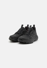 Schwarze Sportschuhe verfügen über ein strukturiertes Obermaterial, eine verstärkte Zehenpartie und eine robuste Gummisohle mit tiefen Profilrillen. Enthält Ziehlaschen für ein einfaches An- und Ausziehen.