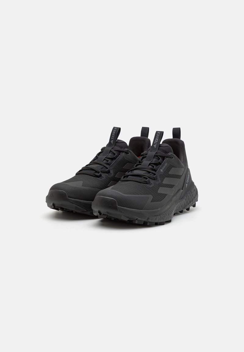 Schwarze Sportschuhe verfügen über ein strukturiertes Obermaterial, eine verstärkte Zehenpartie und eine robuste Gummisohle mit tiefen Profilrillen. Enthält Ziehlaschen für ein einfaches An- und Ausziehen.