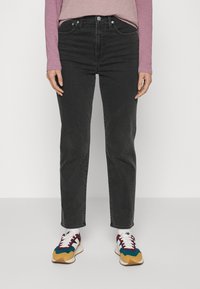 Černé džínové kalhoty s přímým střihem nohavic, s pěti kapsami a klasickým zapínáním na knoflíky. Nošeny s barevnými teniskami a dlouhým rukávem trička.