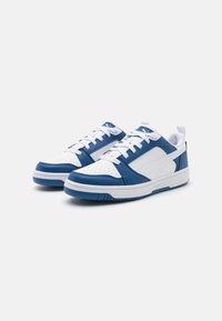 Blauwe en witte sneakers met een bovenkant van leer en synthetisch materiaal, geperforeerde teenbox, witte veters en een prominent logo aan de zijkant.