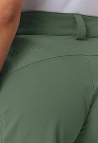 Grüne Vaude-Shorts mit glatter Textur, ausgestattet mit einem Bund und einem eingeprägten Logo an der Seite. Entworfen für Komfort und Beweglichkeit.