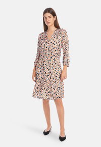 Floral dress with a black background, featuring orange and white flowers, V-neckline, and three-quarter sleeves; ruffled hem. Black shoes.