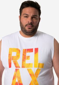 Witte mouwloze shirt met grote "RELAX" in een gradient van oranje en gele letters. Gladde stoftextuur met een ronde halslijn.