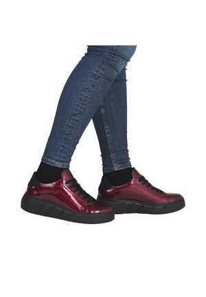 Legs wearing tight blue jeans and black socks, stepping forward in shiny dark red sneakers with thick black soles and laces.