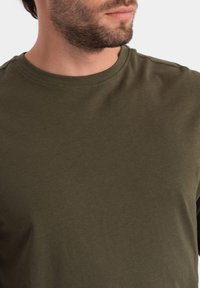 Olivengrünes Langarm-T-Shirt mit Rundhalsausschnitt, aus weichem, glattem Stoff, mit figurnahem Schnitt und minimalen Nähdetails.