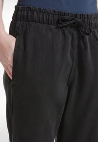 I pantaloni neri con coulisse presentano una vestibilità comoda, una vita elastica, tasche laterali e un tessuto leggermente strutturato.