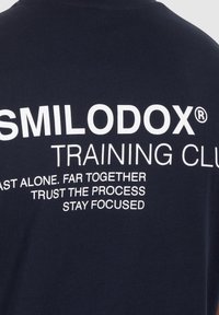 Camiseta de algodón azul marino con texto blanco audaz: "SMILODOX® TRAINING CLUB" con frases motivacionales debajo, diseño de corte recto.