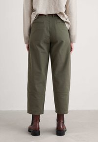 Pantalons cropped verts olive en tissu solide, dotés de poches arrière et de coutures. Portés avec un pull léger et des bottes marron.