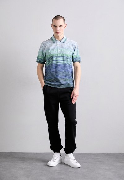 Vīriešu polo krekls ar gradienta zilu-zaļu svītru rakstu, īsām piedurknēm, ar apkakli un trim pogām, apvienots ar melnām sporta biksēm un baltām kedām.