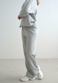 Grå sweatshirt og matchende sweatpants lavet af blødt stof, med en afslappet pasform og minimale sømme. Skoene er hvide med en tekstureret overflade.