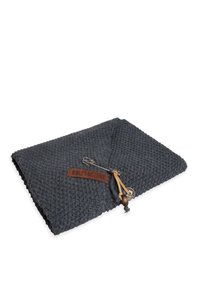 Ciemnoszara, wydziergana narzuta o teksturowanym wzorze, oznaczenie marki, skórzany akcent i przymocowana ozdobna szpilka. Prostokątna forma, złożona.