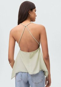 Light green sleeveless top with a back tie design, featuring a slightly flared hem and contrasting stitching details, worn over high-waisted jeans.