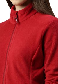 Giacca in pile rossa con colletto alto, zip intera e tessuto testurizzato, dotata di un logo sul tirazip e dal design aderente.