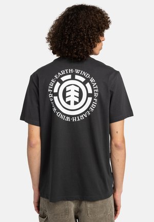 Sort bomulds t-shirt med et stort cirkulært hvidt grafisk print på ryggen med symboler for jord, vind, vand og ild. Korte ærmer.