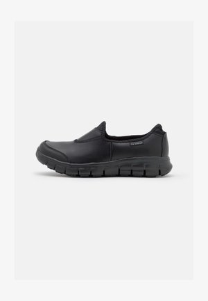 Schwarze Slipper aus glattem Leder, mit gepolstertem Innenraum und strukturierter Gummisohle, die abwechselnd erhöhte Segmente aufweist.