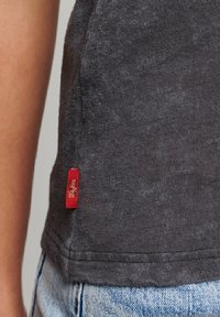 Harmaa t-paita, joka on valmistettu pehmeästä kankaasta, jossa on teksturoitu pinta. Sivureunassa on pieni punainen etiketti. Yksinkertainen leikkaus, ei erottuvia kuvioita.