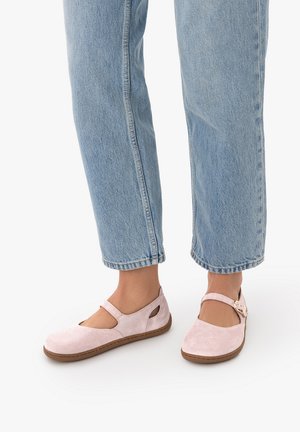 Füße tragen hellrosa Wildleder Mary Jane Ballerinas mit Schnallenriemen und hellblaue Jeans mit geradem Schnitt vor weißem Hintergrund.