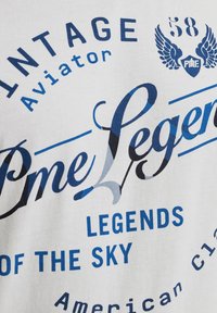 Bijela pamučna majica s plavim grafičkim tekstom. Dizajn uključuje "Vintage Aviator", "Legends of the Sky" i dekorativne akcentne.
