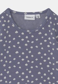 Camisa roxa de mangas curtas com um padrão de bolinhas brancas. Feita de tecido macio, com decote redondo e etiqueta que indica o tamanho 1-2 anos.