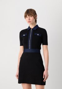 Robe noire à manches courtes, col en denim et poches accentuées, fermeture éclair argentée sur le devant, et une ceinture en denim assortie ; texture de tissu lisse.