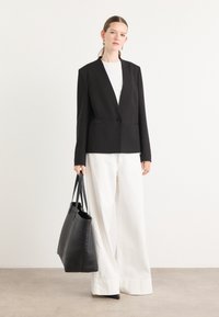 Blazer nero su misura con un unico bottone, abbinato a una t-shirt bianca e pantaloni bianchi a gamba larga. Borsa a mano nera in pelle. Texture liscia.