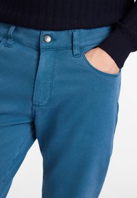 Blaue Baumwollmischung-Hosen mit strukturiertem Finish, ausgestattet mit einem Knopfverschluss, einer Vordertasche und Gürtelschlaufen.