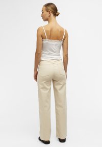 Hvid camisole med blondekant, parret med høj talje beige lige bukser. Glat tekstur, minimalistisk design og to baglommer.